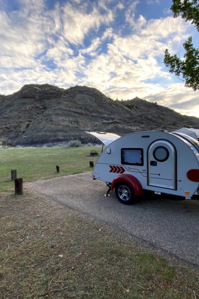 A teardrop trailer at a camp site in front of mountains