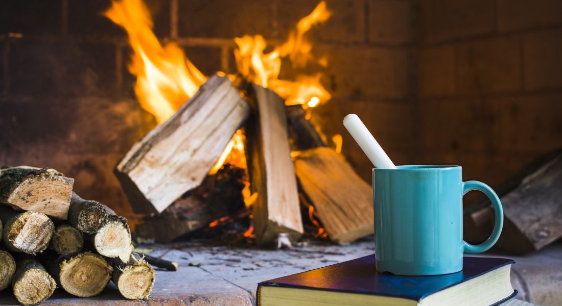 Fire in a fireplace with a cup of tea in front of it on top of a book.